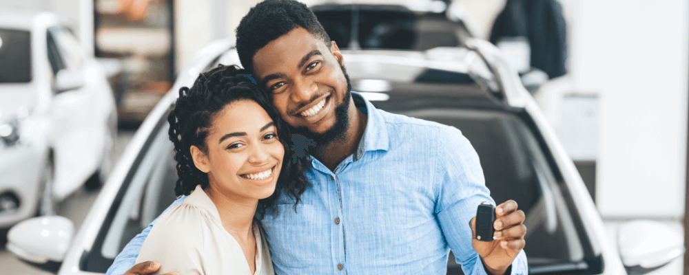 A man and a woman pose for a photo with the key to their new car